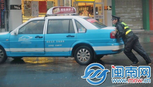 一名协警奋力推车,帮助的哥将车辆移走