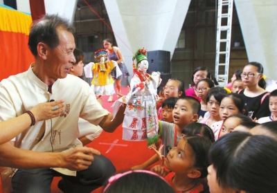 南安市掌中木偶传承人黄通行指导小学生操演木偶。　