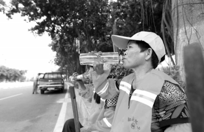 酷暑难耐，清洁工在小憩时为自己补充水分。本报记者