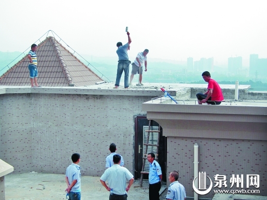 执法人员组织工人对高层楼顶的违法建筑进行拆除